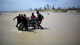 Sejumlah pria membantu warga menggotong sepeda motornya menyeberangi sungai di Les Anglais, 10 Oktober 2016. Selain merusak ribuan rumah, badai Matthew di Haiti juga memutus jembatan yang merupakan akses utama warga. (REUTERS/Andres Martinez Casares)