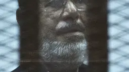 Mantan Presiden Mesir Mohammed Morsi berdiri di belakang jeruji besi saat menjalani sidang di Kairo, Mesir, 16 Juni 2015. Sumber medis setempat mengatakan sosok yang juga memimpin Ikhwanul Muslimin itu meninggal karena serangan jantung mendadak. (Khaled DESOUKI/AFP)