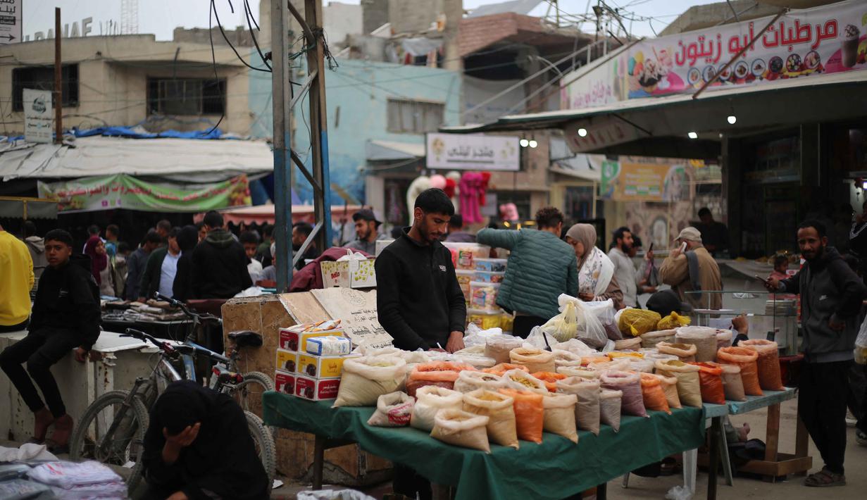 Jumlah pengungsi tersebut terjadi akibat serangan militer Israel menghantam sejumlah wilayah di Gaza sejak Oktober 2023 lalu. Tampak dalam foto, warga Palestina yang mengungsi berbelanja di kios-kios pasar jalanan sekitar kamp pengungsi Nuseirat, Jalur Gaza tengah, pada Rabu 18 Maret 2026. (Eyad Baba/AFP)