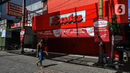 Warga berjalan Suasana di depan pertokoan kawasan perdagangan Pasar Baru yang tutup, Jakarta, Jumat (3/4/2020). Sebagian pemilik toko di Pasar Baru memilih menutup usahanya sementara waktu untuk mengantisipasi meluasnya penyebaran virus corona COVID-19. (Liputan6.com/Faizal Fanani)