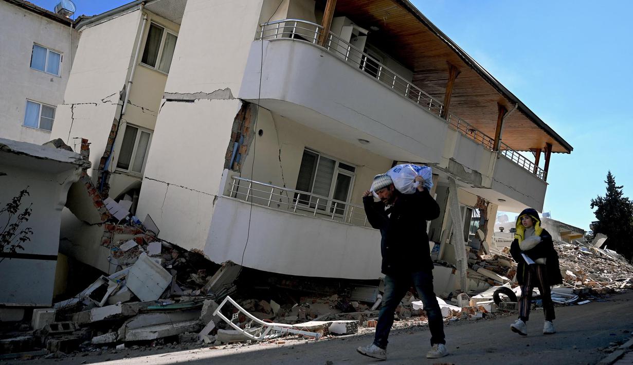 Orang-orang berjalan di sebuah jalan melewati sebuah bangunan yang rusak, setelah gempa berkekuatan 7,8 magnitudo yang melanda beberapa wilayah di Turki dan Suriah, Kamis 16 Februari 2023. (OZAN KOSE/AFP)