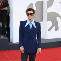Harry Styles memakai setelan biru bercelana flared kemeja sutra biru muda berkerah runcing. Serta sepatu bot kuli putih dari Gucci HA HA HA plus kacamata cokelat bingkai persegi untuk melengkapi ansambelnya di premiere 'Don't Worry Darling' (Foto: Gucci)