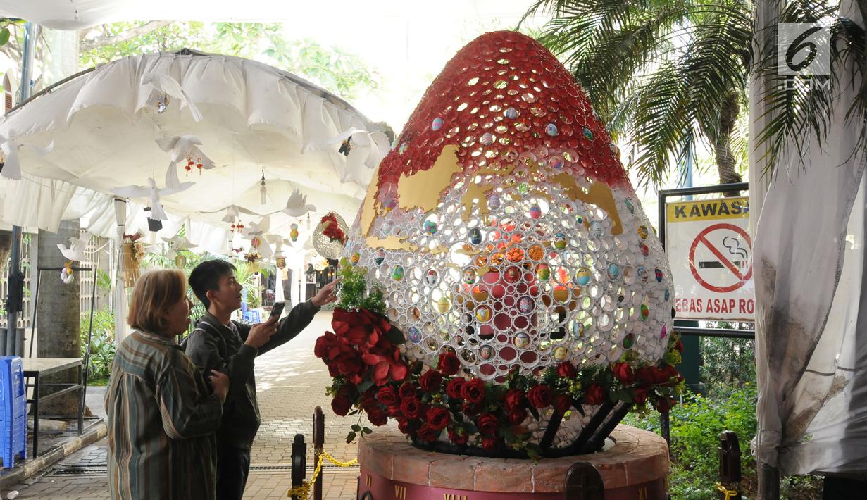 Warga melihat hiasan telur paskah yang ada pada dekorasi telur paskah raksasa di Gereja Katedral, Jakarta, Minggu (4/1). Hiasan pada telur telur paskah tersebut mewarnai perayaan Paskah di Gereja Katedral. (Liputan6.com/Helmi Fithriansyah)