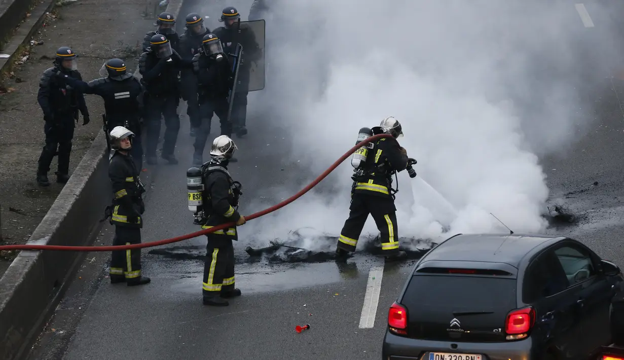 Pemadam kebakaran memadamkan api dari ban yang dibakar pengemudi taksi saat unjuk rasa menentang layanan transportasi VTC seperti Uber, di jalan lingkar di porte Maillot di Paris, Perancis, Selasa (26/1). (AFP PHOTO/Thomas SAMSON)