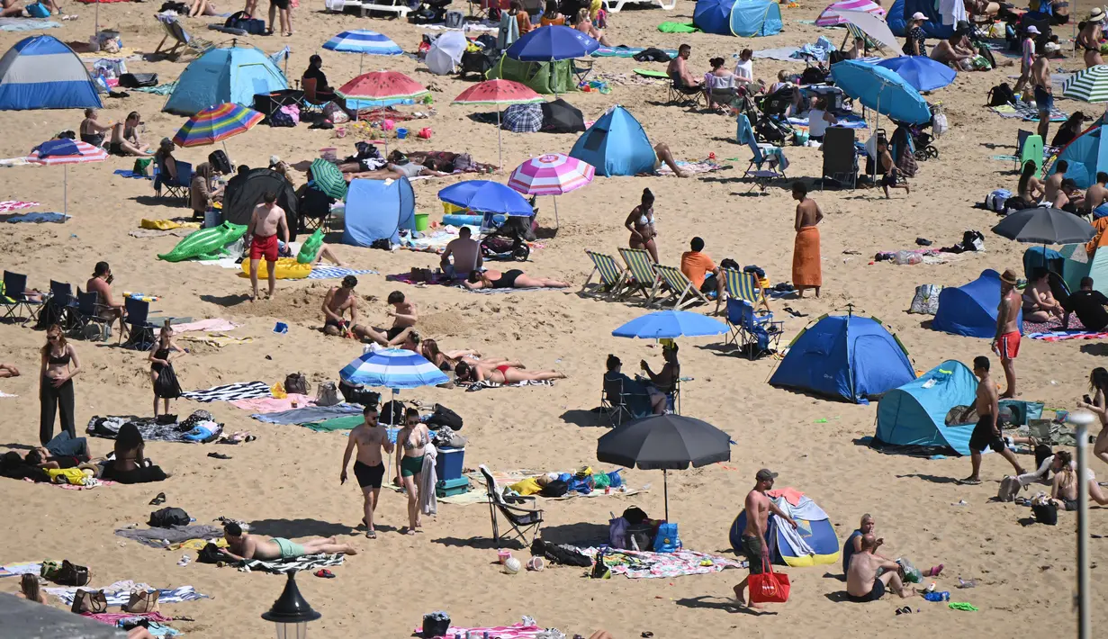 Para pengunjung berjemur menikmati sinar matahari di Pantai Bournemouth, Selatan Inggris pada Selasa 26 Mei 2026, saat kondisi gelombang panas menyebar ke sebagian wilayah tenggara Inggris dan London. (JUSTIN TALLIS/AFP)