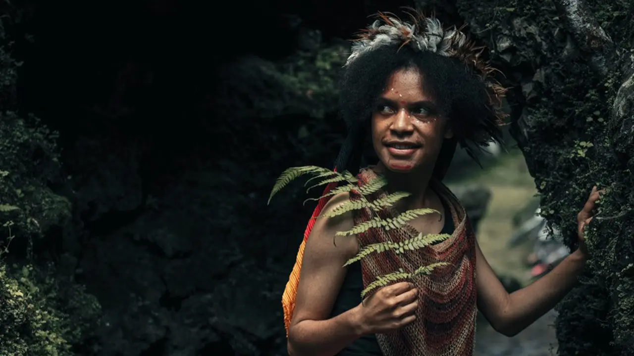 Closeup gadis muda eksotis suku dani papua dengan pakaian tradisional tersenyum di tengah hutan.