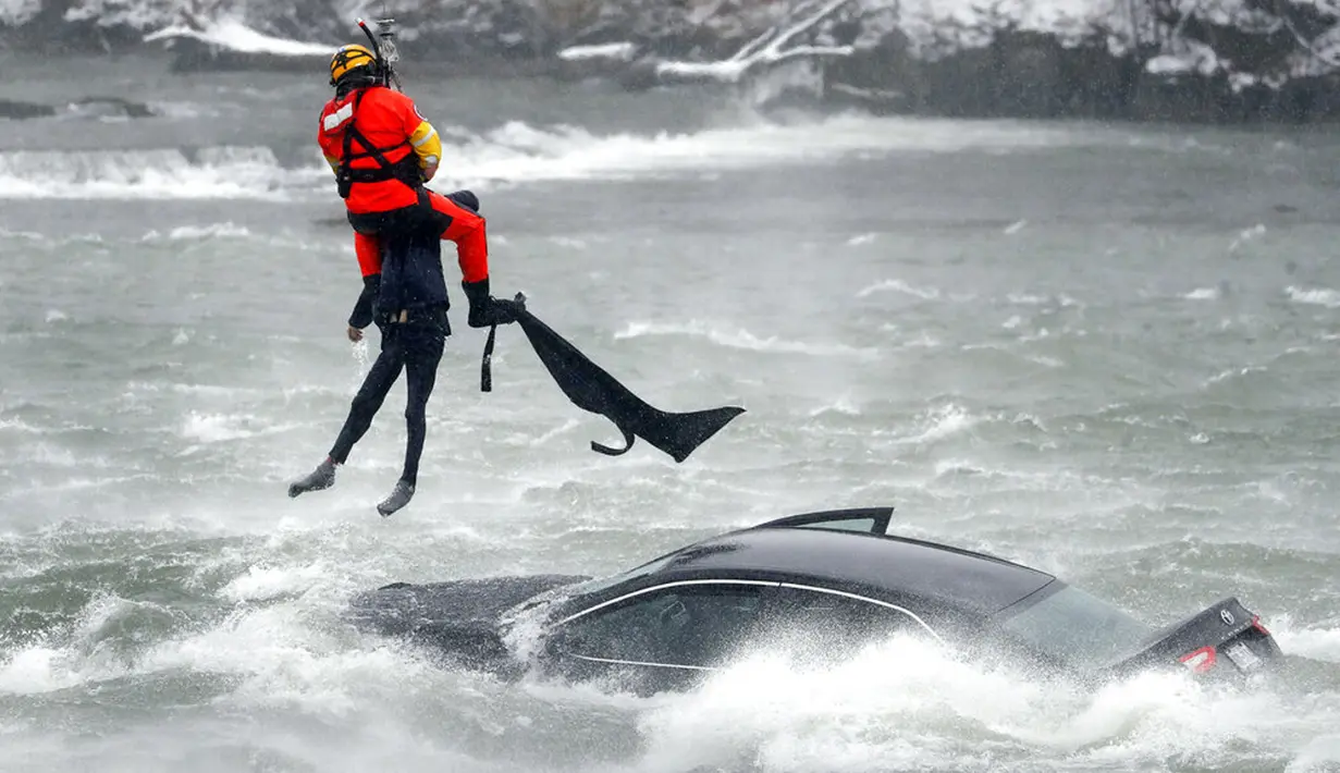 Penyelam Penjaga Pantai AS yang ditambatkan pada helikopter menarik tubuh pengendara mobil yang terjebak dalam arus deras di tepi Air Terjun Niagara, New York, AS, 8 Desember 2021. Wanita berusia 66 tahun meninggal setelah terjebak dua jam dalam air beku. (Sharon Cantillon/The Buffalo News via AP)