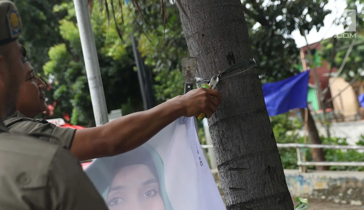 Petugas Satpol PP mencabut paku yang digunakan untuk memasang APK yang terpasang di Jalan Raya Bogor dekat GOR Ciracas, Jakarta, Rabu (23/1). Penurunan APK ini karena pemasangannya dianggap melanggar ketentuan. (Liputan6.com/Helmi Fithriansyah)