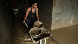 Upaya pembersihan dilakukan di tengah keterbatasan pasokan air bersih. Tampak dalam foto, Panji (23 tahun) membawa lumpur keluar dari dapur menggunakan gerobak dorong di rumah orang tuanya di Aceh Tamiang, Minggu 14 Desember 2025. (Yasuyoshi CHIBA/AFP)