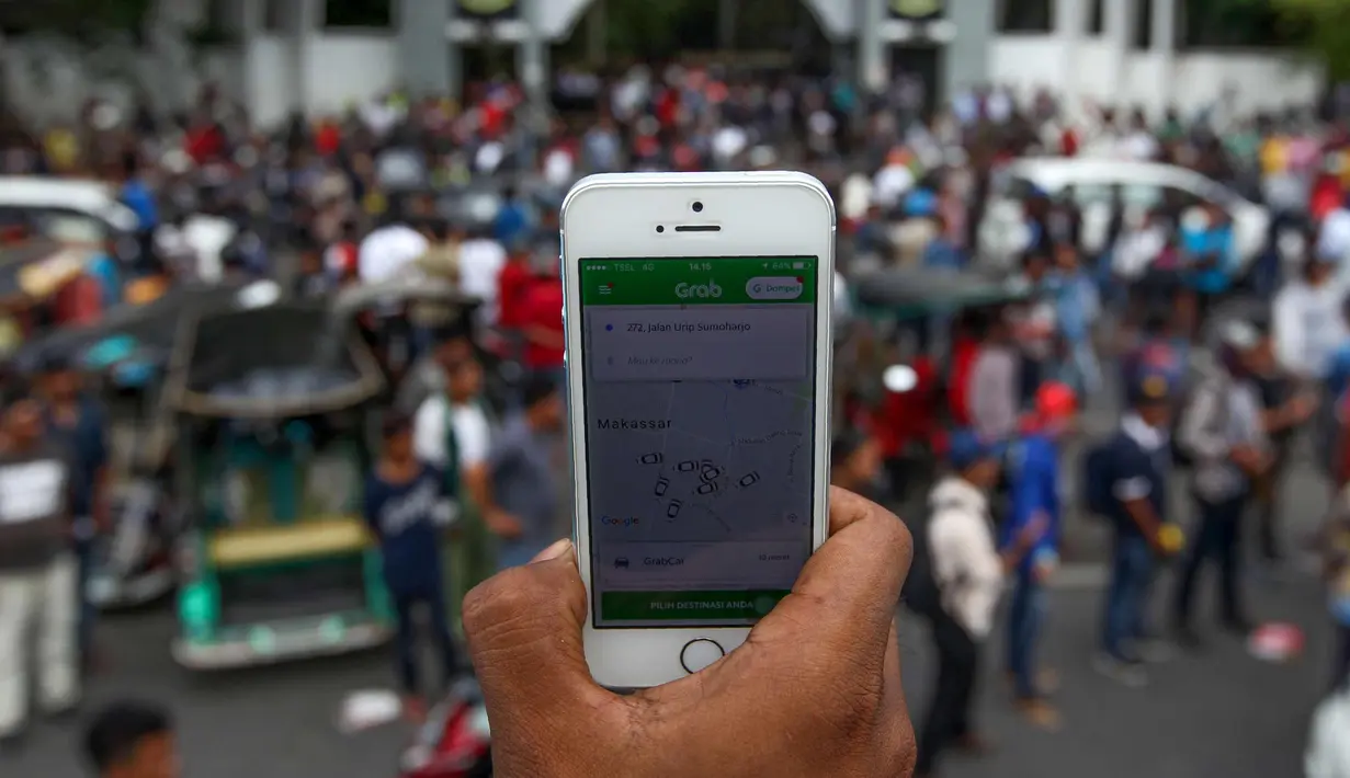 Pendemo menunjukkan aplikasi transportasi online saat unjuk rasa di Makassar, Rabu (1/11). Mereka menggeruduk kantor Gubernur Sulsel untuk menuntut maraknya transportasi online yang dianggap memakan rezeki mereka. (AFP Photo/Yusuf Wahil)