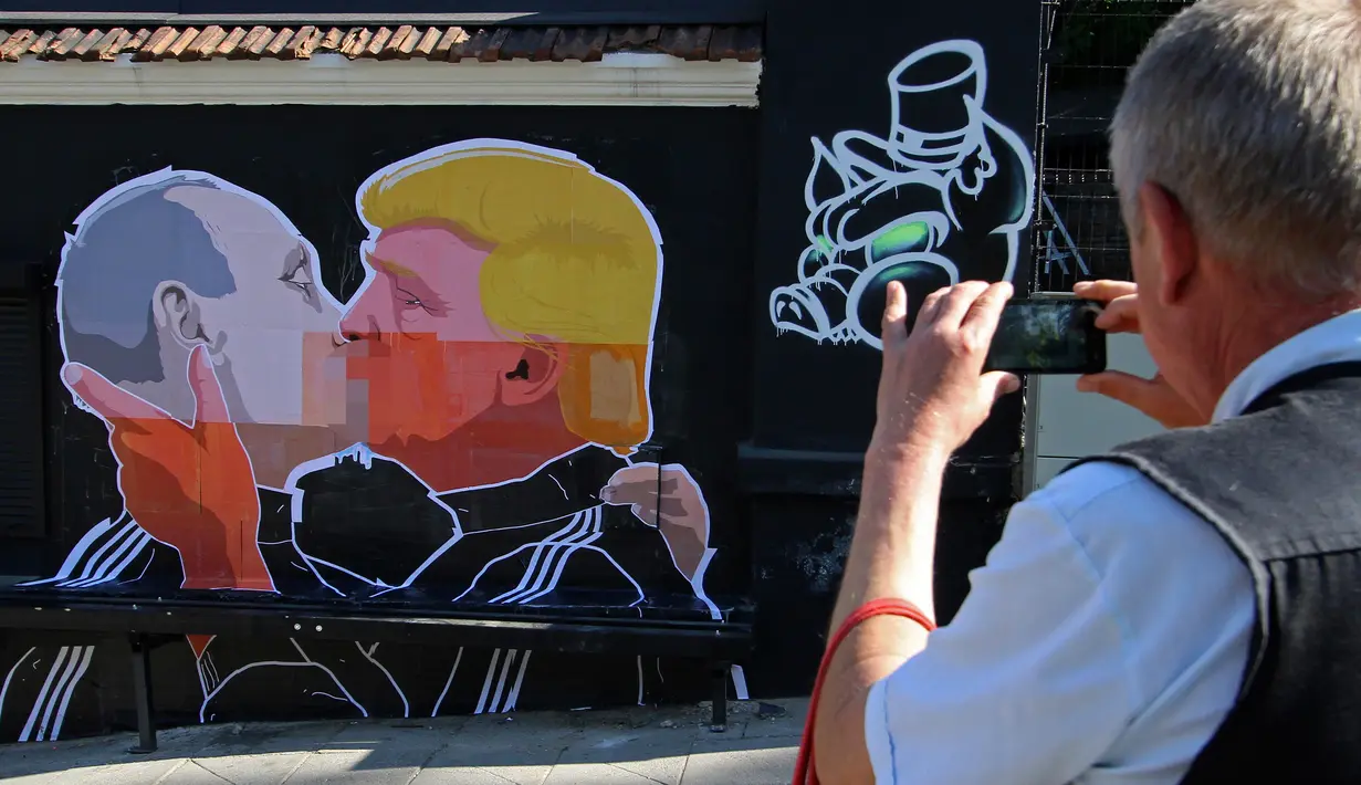 Warga mengabadikan mural bergambar calon Presiden AS, Donald Trump dan Presiden Rusia, Vladimir Putin sedang berciuman di Vilnius , Lithuania, (13/5). Mural ini dibuat sebagai sindiran terhadap Donald Trump dan Vladimir Putin. (AFP PHOTO/Petras Malukas)