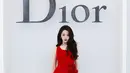 Dilraba mencuri perhatian dengan gaun beludru merah asimetris. Dihiasi bros bunga besar di pinggang, dipadukan tas Lady Dior hitam dan heels bermotif bunga merah [dok. Dior]