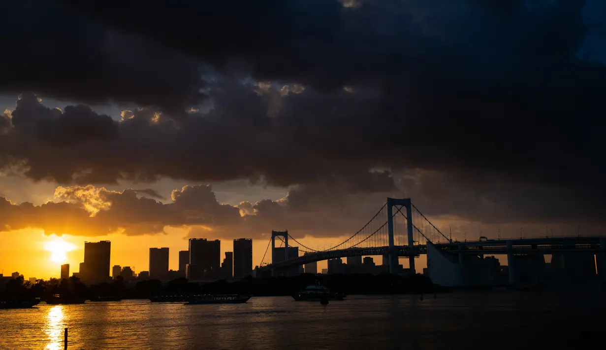 The Rainbow Bridge terlihat saat matahari terbenam di Tokyo, Jepang (29/7). Odaiba merupakan salah satu tujuan wisata di Tokyo, sekaligus lokasi pusat perbelanjaan dan permukiman. (AFP Photo/Martin Bureau)