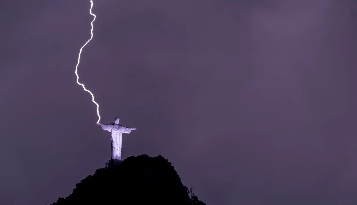 Petir menyambar tangan Christ the Redeemer atau Patung Kristus Penebus di gunung Corcovado di Rio de Janeiro, Brasil, Selasa (21/2/2023). Tingginya patung juga membuatnya beberapa kali tersambar petir saat badai menerjang kota tersebut. (Photo by MAURO PIMENTEL / AFP)
