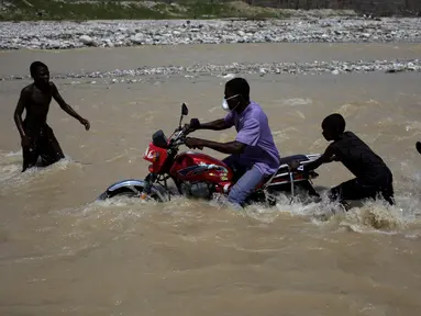Bocah laki-laki membantu pengendara sepeda motor yang berusaha menyeberangi sungai di Les Anglais, 10 Oktober 2016. Selain merusak ribuan rumah, badai Matthew di Haiti juga memutus jembatan yang biasa digunakan warga. (REUTERS/Andres Martinez Casares)