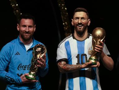 Bintang sepak bola Argentina, Lionel Messi, memegang replika trofi Piala Dunia FIFA di samping patung dirinya dalam sebuah upacara untuk menghormati skuad Argentina setelah mereka menang Piala Dunia, di markas besar CONMEBOL di Asuncion, Paraguay, Senin (27/3/2023). (AP Photo/Jorge Saenz)