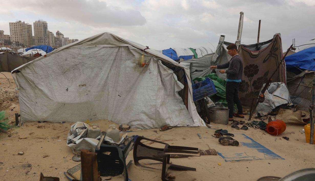 Kondisi ini semakin memperburuk situasi kemanusiaan yang telah kritis dan memicu kekhawatiran akan bencana yang kian mendalam. Tampak dalam foto, seorang pria Palestina yang mengungsi memperbaiki tenda yang didirikan di sepanjang pantai Kota Gaza saat angin musim dingin yang kencang menerpa wilayah tersebut pada Selasa 13 Januari 2026. (Omar AL-QATTAA/AFP)