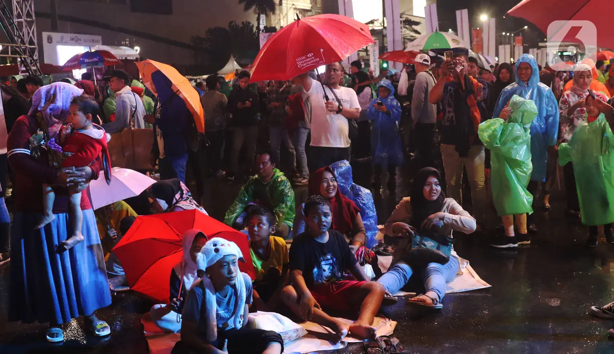 Masyarakat beristirahat saat car free night di kawasan Thamrin, Jakarta, Selasa (31/12/2019). Meski diguyur hujan masyarakat mulai memadati kawasan tersebut untuk menikmati malam pergantian tahun 2019. (Liputan6.com/Angga Yuniar)
