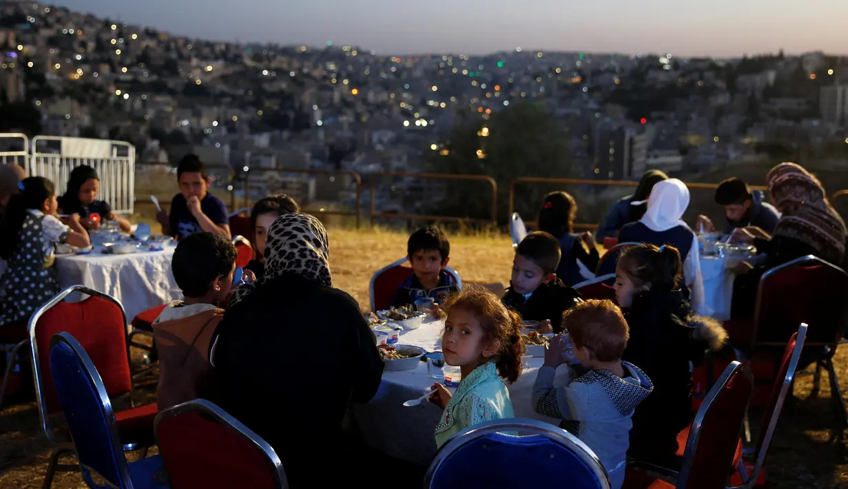 Sekelompok anak yatim dari kota utara Irbid berbuka puasa setelah menyaksikan penembakan meriam sebagai tanda berbuka puasa di Benteng Amman, 13 Mei 2019. Saat tiba waktu Maghrib yang sekaligus menjadi penanda waktu berbuka puasa di Yordania, ditandai dengan tembakan meriam. (REUTERS/Muhammad Hamed)