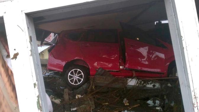 Sebuah mobil yang tersapu oleh tsunami terlihat terjebak di bawah bangunan yang rusak di Palu, Sulawesi Tengah , Sabtu (29/9). Gelombang tsunami yang menerjang Palu terjadi setelah gempa bumi mengguncang Palu dan Donggala. (Dede Budiyarto via AP)