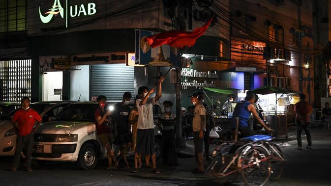 Orang-orang mengibarkan bendera partai Liga Nasional untuk Demokrasi (NLD) dan menyalakan ponsel mereka setelah seruan untuk protes keluar di media sosial di Yangon, Myanmar, 3 Februari 2021. Kudeta militer Myanmar terus memicu protes warga. (STR/AFP)