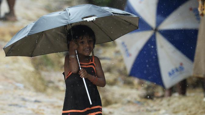 Seorang anak pengungsi Rohingya berjalan menggunakan payung saat hujan di kamp pengungsi Kutupalong, Ukhia (12/9/2019). Kamp ini didirikan secara tidak resmi pada tahun 1991, setelah ribuan orang Rohingya melarikan diri dari Operasi Pyi Thaya yang dilancarkan militer Burma. (AFP Photo/Munir Uz Zaman