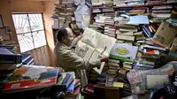 Jose Alberto Gutierrez membaca koran tua di antara koleksi buku di perpustakaan rumahnya di Bogota, 18 Mei 2017. Meski awalnya Gutierrez menemukan buku dari tumpukan sampah, sebagian besar buku yang ia koleksi kini adalah sumbangan (GUILLERMO LEGARIA/AFP)