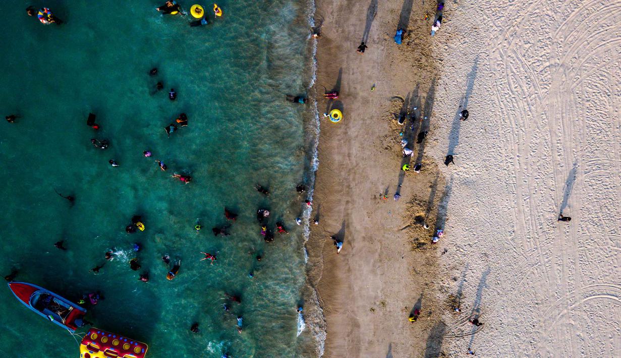 Dengan hamparan pasir putih yang lembut, air laut yang jernih, dan ombak yang memikat, pantai ini menawarkan keindahan alam yang luar biasa. Tampak foto udara menunjukkan orang-orang saat berkumpul menikmati masa libur panjang Idulfitri di area olahraga air, Pantai Lhoknga, Aceh, pada Kamis 26 Maret 2026. (Chaideer MAHYUDDIN/AFP)
