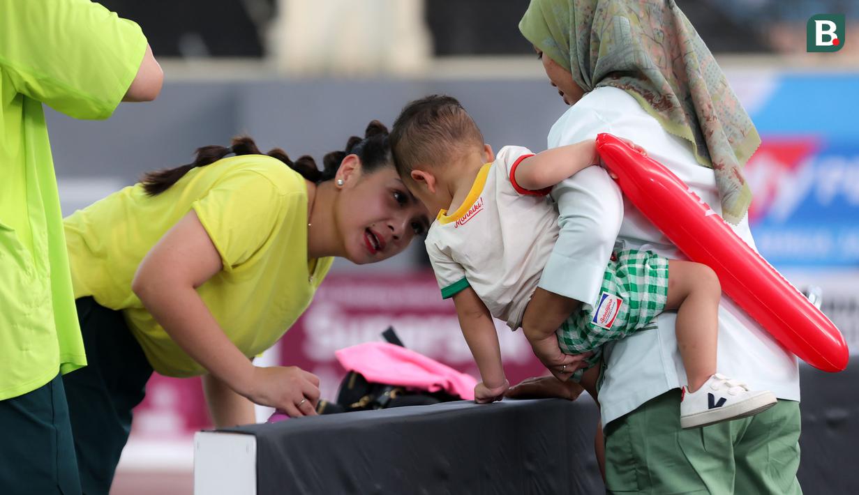 Selebritas Nagita Slavina (kiri) mendatangi putranya, Rayyanza Malik Ahmad atau yang akrab disapa Cipung saat laga tenis nomor ganda campuran Turnamen Olahraga Selebriti Indonesia (TOSI) yang digelar di GOR UNJ, Jakarta, Sabtu (15/07/2023). Gigi, sapaan Nagita Slavina, yang berpasangan dengan Ritchie Ismail atau dikenal sebagai Jeje Govinda kalah dari pasangan Gege dan Ibnu Jamil dua set langsung  (5-7, 6(2)-7(7)). (Bola.com/Abdul Aziz)