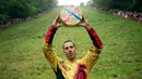 Chris Anderson memegang hadiah setelah berhasil memecahkan rekor dalam kompetisi Cheese Rolling di Cooper's Hill di Brockworth, Gloucestershire, Inggris, Senin (28/5). (Aaron Chown/PA via AP)
