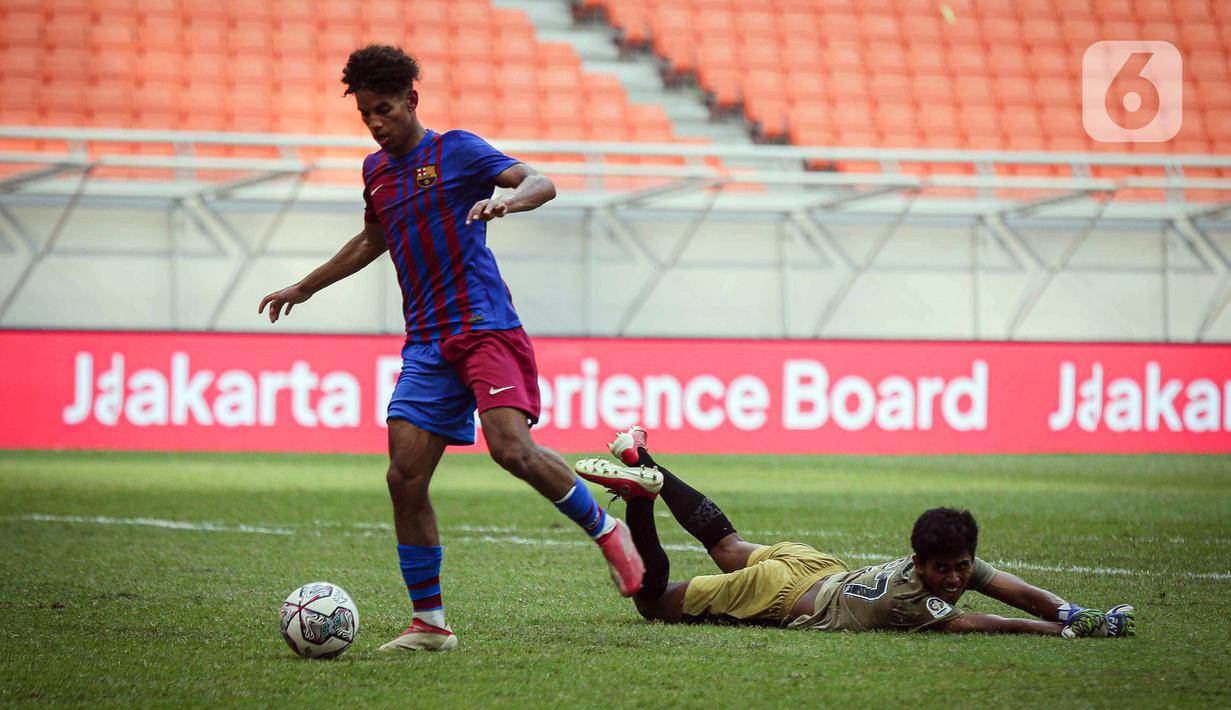 Pemain Barcelona U-18 Jorge Javier Espinal Díaz (kiri) menggiring bola melewati kiper Bali United U-18 I Komang Aryantara pada pertandingan International Youth Championship (IYC) 2021 di Jakarta International Stadium (JIS), Jakarta, Minggu (17/4/2022). (Liputan6.com/Faizal Fanani)