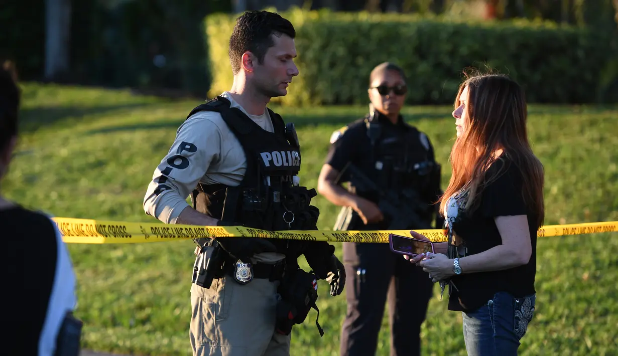 Seorang wanita bertanya kepada petugas kepolisian yang berjaga di lokasi penembakan massal sekolah menengah atas di Parkland, Florida, Rabu (14/2). Pelaku, Nikolaus Cruz (19), menembaki rekannya sesama siswa menggunakan senapan serbu AR-15. (AP PHOTO)