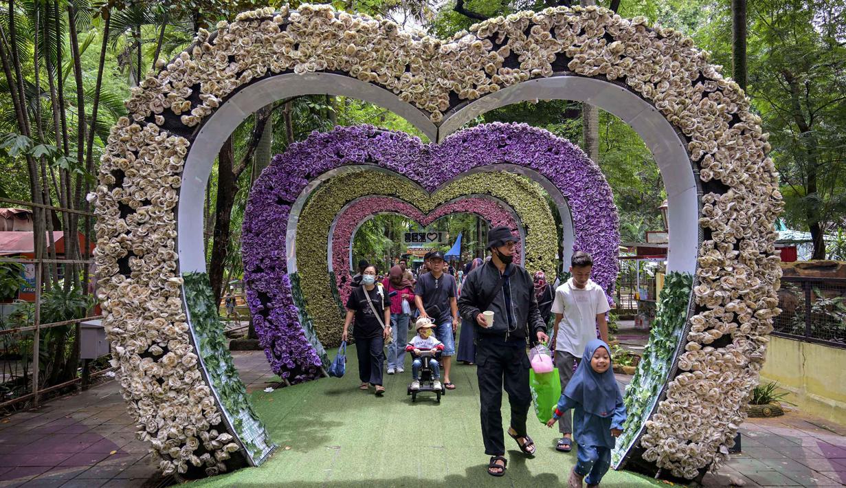 Meski peningkatan jumlah kunjungan sempat melambat akibat cuaca hujan, namun secara keseluruhan, pengelola Kebun Binatang Surabaya (KBS) menargetkan kenaikan jumlah pengunjung sebesar 10-15 persen selama periode libur sekolah dan Nataru 2025. Tampak dalam foto, pengunjung berjalan melewati dekorasi berbentuk hati di Kebun Binatang Surabaya, Jawa Timur, selama libur sekolah sekaligus jelang Natal dan Tahun Baru pada Minggu 21 Desember 2025. (JUNI KRISWANTO/AFP)