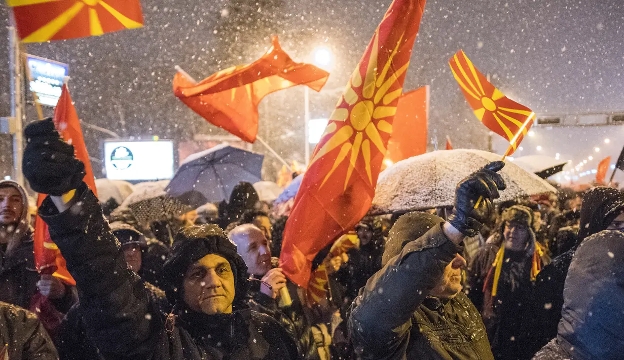 Pengunjuk rasa mengibarkan bendera Macedonia saat menggelar protes di depan gedung Parlemen, Skopje, Selasa (27/2). Di tengah hujan salju, mereka turun ke jalan memprotes wacana pengubahan nama negara mereka. (Robert ATANASOVSKI/AFP)