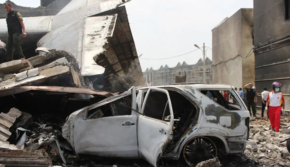 Sebuah mobil yang hangus terbakar tertimpa ekor pesawat Hercules C-130 yang jatuh di kawasan perumahan di Medan, Selasa (30/6/2015). Diperkirakan sekitar 50 penumpang berada dalam pesawat untuk melakukan rotasi tugas piket. (AFP PHOTO/ATAR)