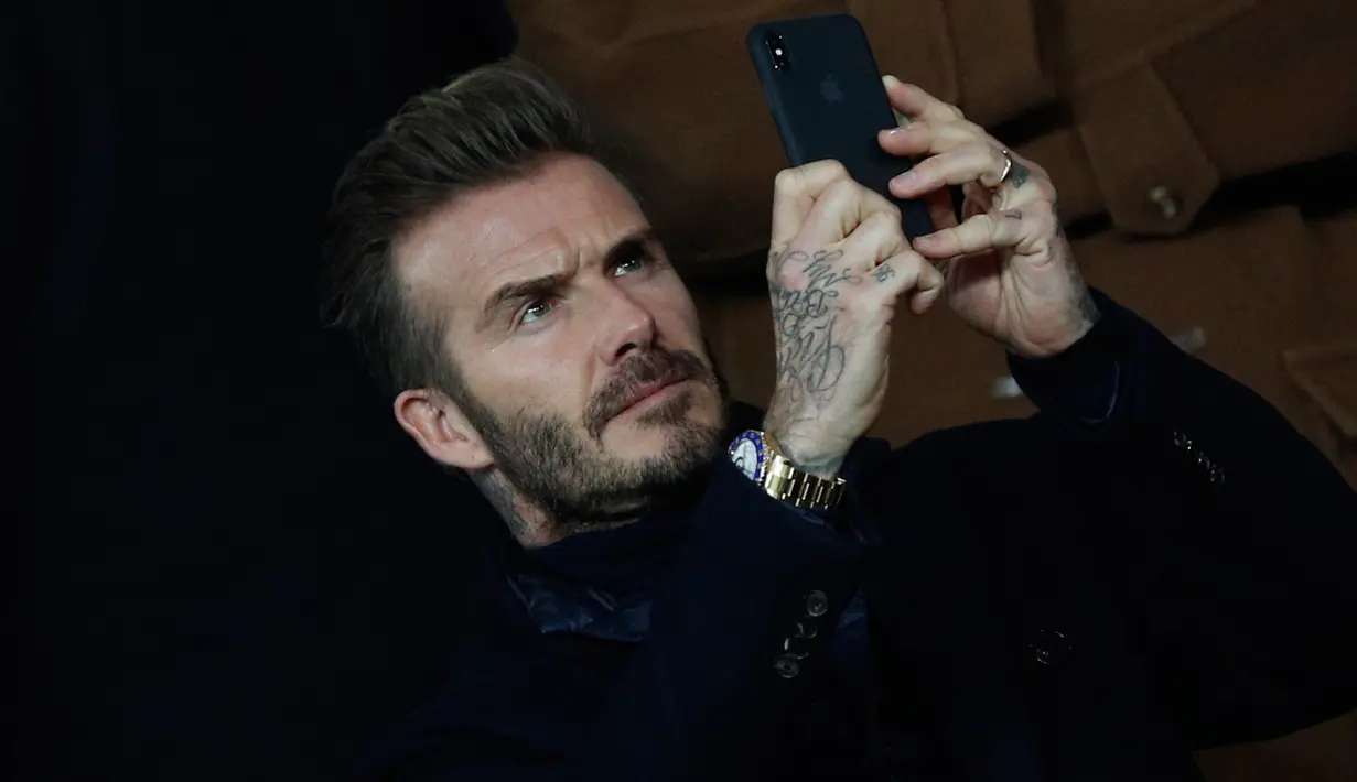 David Beckham mengambil gambar saat menonton pertandingan antara PSG dan Real Madrid di stadion Parc des Princes di Paris (6/3). David Beckham, yang pernah berkostum Madrid dan PSG juga turut hadir menonton pertandingan. (AP Photo/Christophe Ena)