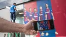 Seorang pria menunjukkan foto di ponselnya yang menampilkan poster pemain depan Barcelona Neymar (kedua kanan) sebelum diganti dengan poster yang terbaru di luar Stadion Camp Nou di Barcelona (2/8). (AFP Photo/Josep Lago)