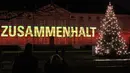 Pengunjung menikmati pemandangan Istana Bellevue yang diterangi proyeksi cahaya bertuliskan "Zusammenhalt", yang bermakna saling bergandengan tangan, di Berlin, 17 Desember 2020. Pertunjukan cahaya bertema "Lichtblick" ini untuk menyerukan solidaritas demi melawan pandemi COVID-19 (Xinhua/Shan Yuqi)