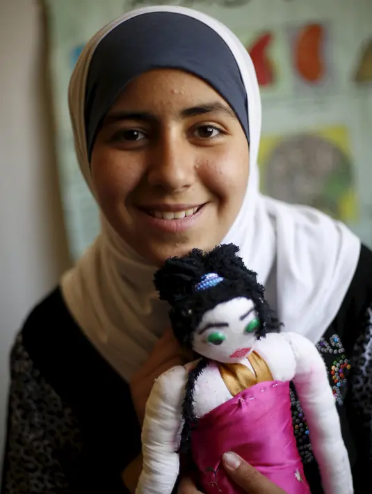 Omayma bersama boneka kesayangannya tersenyum di rumahnya di kamp pengungsi Al Zaatari, Mafraq, Yordania (21/4). Meski berusia 14 tahun, Omayma sangat aktif menyerukan perlawanan terhadap pernikahan dini yang marak di Suriah. (REUTERS / Muhammad Hamed)