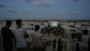 Warga Palestina menyaksikan siaran langsung pertandingan sepak bola Piala Dunia antara Spanyol dan Arab Saudi melalui layer lebar di Nuseirat, Jalur Gaza Tengah, Minggu 21 Juni 2026. (AP Photo/Abdel Kareem Hana)