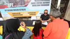 Petugas Unit Pengelola Zakat (UPZ) melayani pembayaran zakat, fidyah, kafarat, infaq, dan shadaqah di teras Masjid Istiqlal, Jakarta, Minggu 15 Maret 2026. Selain menjalankan ibadah selama bulan suci Ramadan, umat muslim juga diwajibkan untuk menunaikan zakat fitrah. (Kapanlagi.com/Budy Santoso)