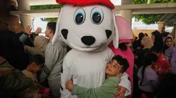 Meski dalam kondisi perang, beberapa pengungsi tetap berupaya menghadirkan kegembiraan, terutama untuk anak-anak, dalam menyambut hadirnya Hari Raya Idulfitri. Tampak dalam foto, seorang anak memeluk seseorang yang mengenakan kostum saat para sukarelawan menyiapkan bingkisan makanan dan manisan Idulfitri untuk keluarga pengungsi yang merayakan hari raya jauh dari rumah mereka, di sebuah universitas negeri yang diubah menjadi tempat penampungan setelah serangan udara Israel di Beirut, Lebanon, Jumat 20 Maret 2026. (AP Photo/Hassan Ammar)