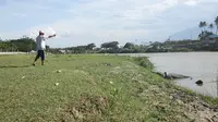Seorang warga memotret buaya berkalung ban yang sedang berjemur di tepi Sungai Palu. BKSDA Sulteng melarang aksi tersebut karena berbahaya. (Foto: Heri Susanto/ Liputan6.com).