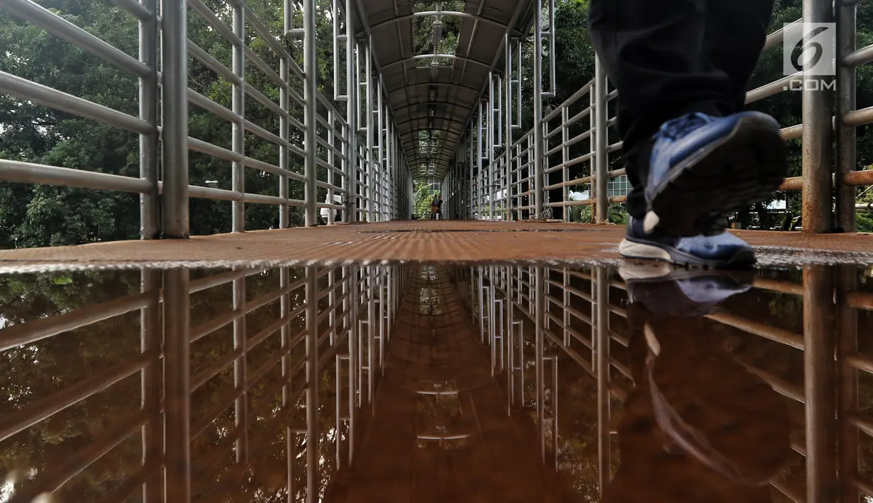 Pejalan kaki melintasi genangan air di JPO Medan Merdeka Barat, Jakarta, Jumat (19/1). Kondisi JPO yang penuh dengan genangan air dan atap yang rusak ini mengurangi kenyamanan bagi para pejalan kaki yang menggunakannya. (Liputan6.com/Johan Tallo)