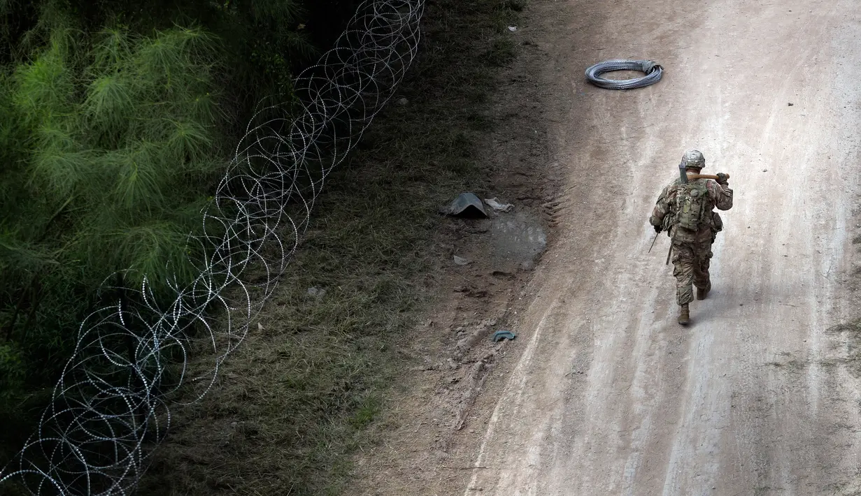 Tentara AS berjalan saat memasang kawat duri di perbatasan AS-Meksiko di Jembatan Internasional McAllen-Hidalgo, Texas, Jumat (2/11). Presiden AS Donald Trump mengatakan kehadiran pasukannya untuk mengantisipasi 'invasi' imigran. (AP Photo/Eric Gay)