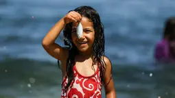 Seorang gadis Palestina tersenyum saat memegang ikan saat bermain bersama teman-temanya di laut Mediterania dekat kamp pengungsi al-Shati di Kota Gaza (3/7). (AFP Photo/Mohammed Abed)