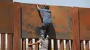 Seorang pemuda dibantu temannya memanjat tembok besi perbatasan antara Meksiko dan Amerika Serikat di negara bagian Chihuahua, Meksiko (6/4). Mereka menyeberang secara ilegal ke Sunland Park dari Ciudad Juarez. (AFP/Herika Matinez)