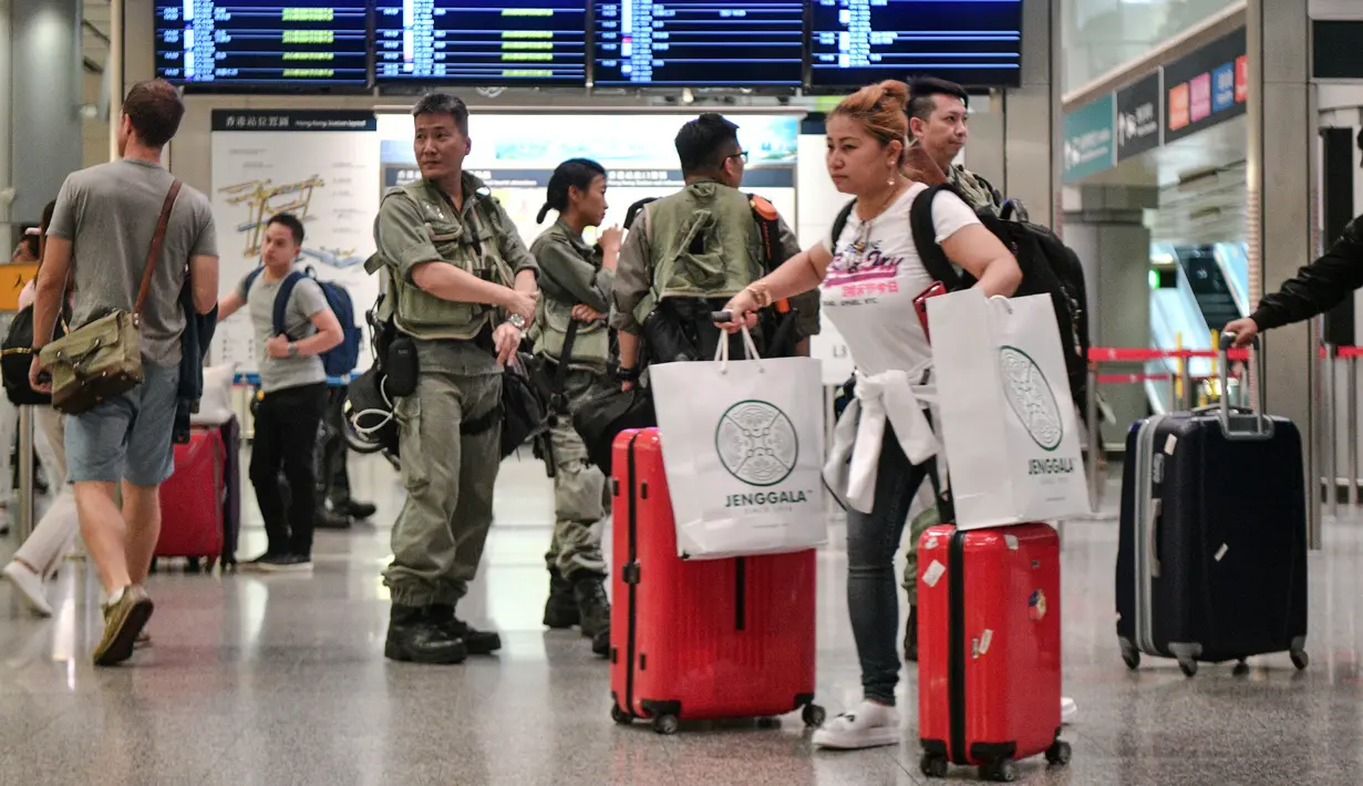 Penumpang melintas saat polisi anti huru-hara berjaga di stasiun Airport Express di Central yang menghubungkan ke Bandara Internasional Chek Lap Kok, Hong Kong (7/9/2019). Pengunjuk rasa pro-demokrasi berencana mengganggu jaringan transportasi ke bandara pada 7 September. (AFP Photo/Anthony Wallace)