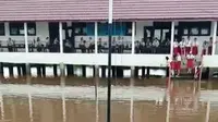 Tiga pelajar SDN 3 Tanah Abang Kabupaten PALI Sumsel mengibarkan bendera di tengah banjir tinggi di lapangan sekolahnya (Liputan6.com / Nefri Inge)