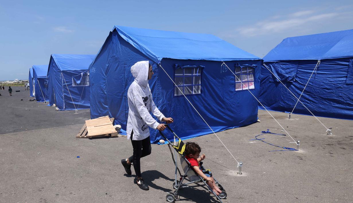 Seorang perempuan Lebanon yang mengungsi mendorong kereta bayi di dekat tenda-tenda biru yang didirikan pemerintah untuk orang-orang yang meninggalkan rumah dan desa mereka di pinggiran selatan Beirut dan Lebanon Selatan, Jumat 22 Mei 2026. (Anwar AMRO/AFP)